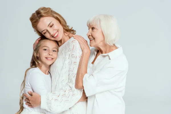 Lächelnde Enkelin, Mutter und Großmutter umarmen sich isoliert auf grau — Stockfoto