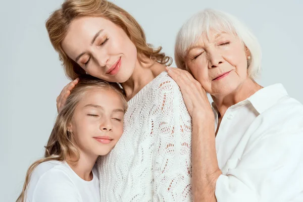 Lächelnde Enkelin, Mutter und Großmutter mit geschlossenen Augen, die sich isoliert auf grau umarmen — Stockfoto