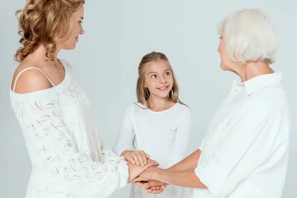 Sonriente madre, abuela y nieta cogidas de la mano aisladas en gris - foto de stock