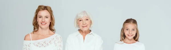 Panoramic shot of smiling granddaughter, mother and grandmother looking at camera isolated on grey — Stock Photo