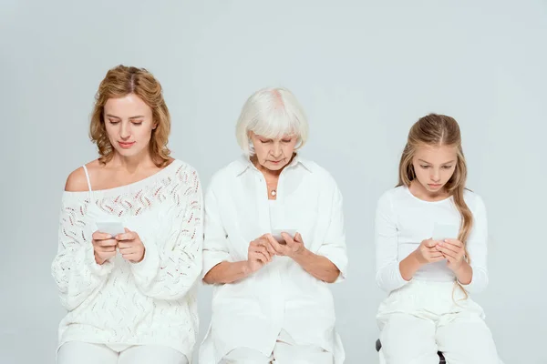 Внучка, мать и бабушка с помощью смартфонов, изолированных на сером — стоковое фото