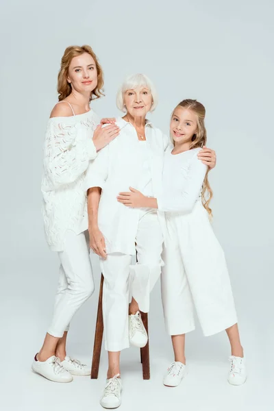 Smiling granddaughter and mother hugging grandmother on grey background — Stock Photo