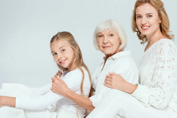 Smiling granddaughter, mother and grandmother hugging isolated on grey — Stock Photo