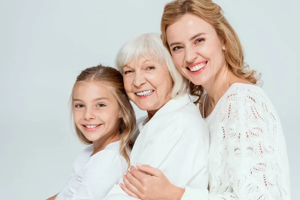 Smiling granddaughter, mother and grandmother hugging isolated on grey — Stock Photo