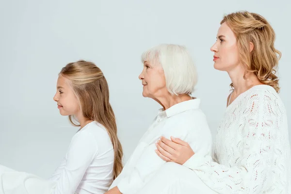 Seitenansicht der lächelnden Enkelin, Mutter und Großmutter, die sich isoliert auf grau umarmen — Stockfoto