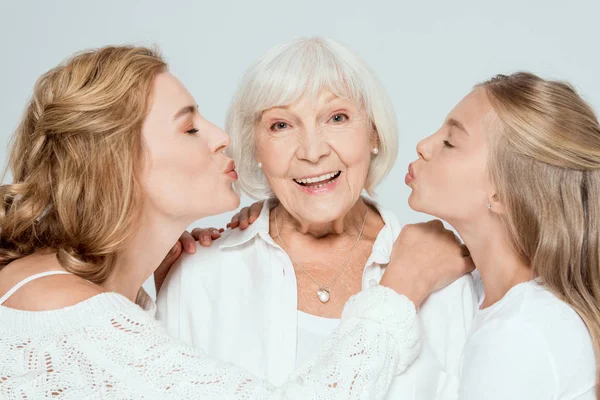 Enkelin und Mutter küssen lächelnde Großmutter isoliert auf grau — Stockfoto