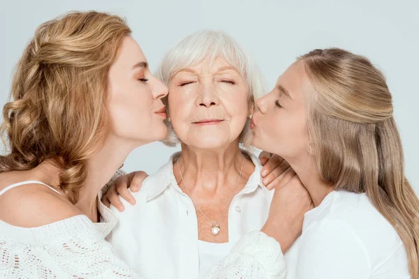 Granddaughter and mother kissing grandmother with closed eyes isolated on grey — Stock Photo