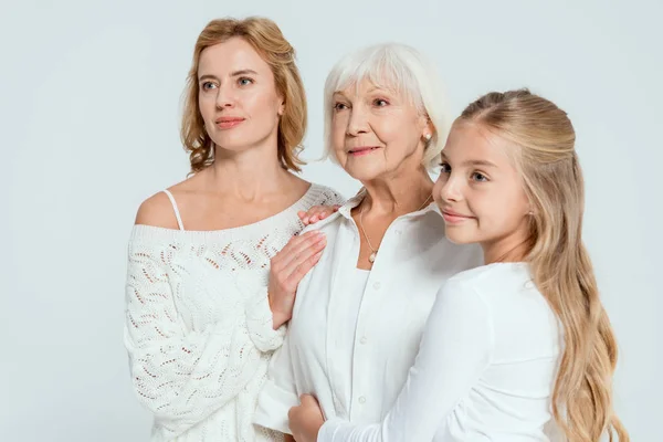 Smiling granddaughter and mother hugging grandmother isolated on grey — Stock Photo