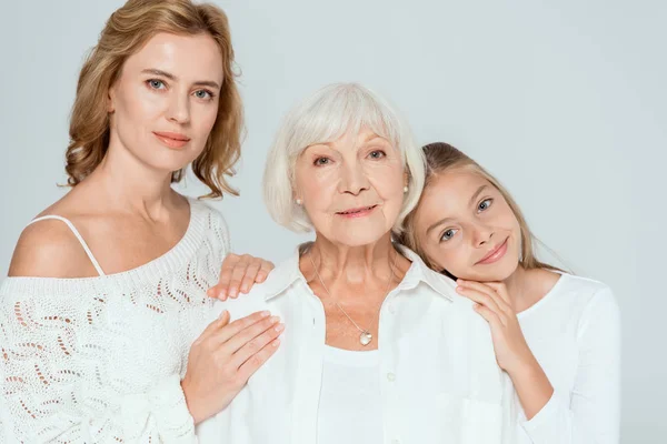 Smiling granddaughter and mother hugging grandmother isolated on grey — Stock Photo