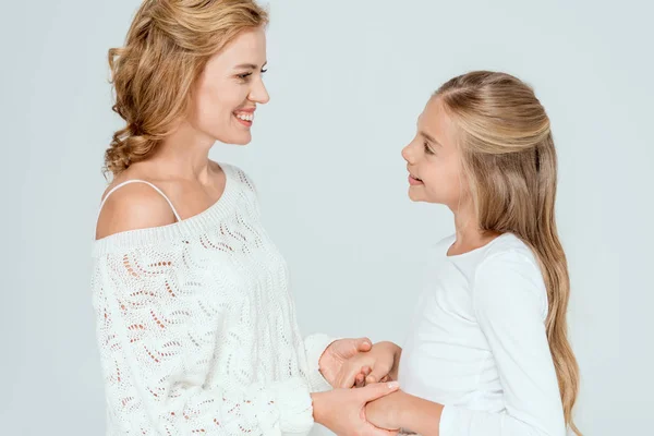 Vista lateral de la atractiva madre y la hija sonriente cogidas de la mano aisladas en gris - foto de stock