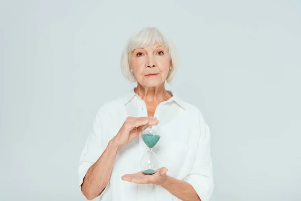 Attractive woman looking at camera and holding hourglass isolated on grey — Stock Photo