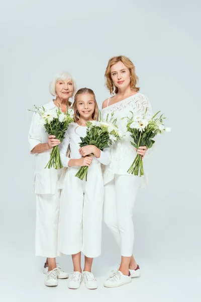 Lächelnde Enkelin, Mutter und Großmutter mit Blumensträußen auf grauem Hintergrund — Stockfoto