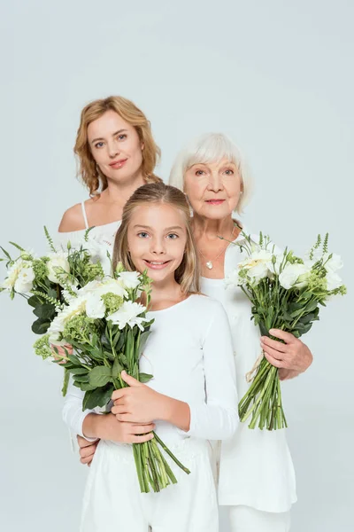 Smiling granddaughter, mother and grandmother holding bouquets isolated on grey — Stock Photo