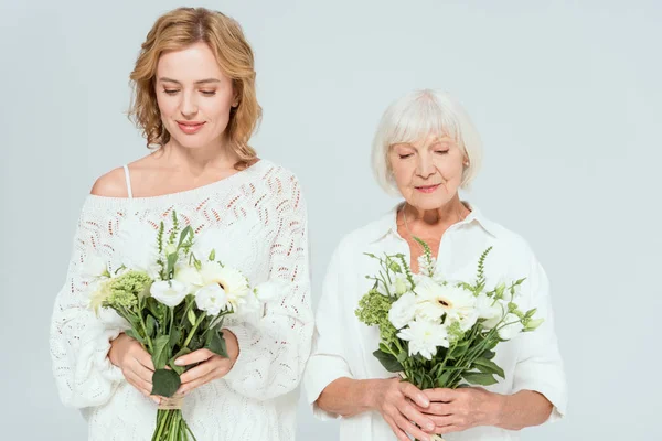 Attractive mother and smiling daughter holding bouquets isolated on grey — Stock Photo