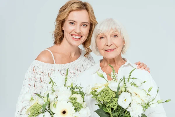 Attractive mother and smiling daughter holding bouquets isolated on grey — Stock Photo