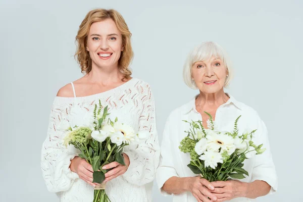 Attractive mother and smiling daughter holding bouquets isolated on grey — Stock Photo