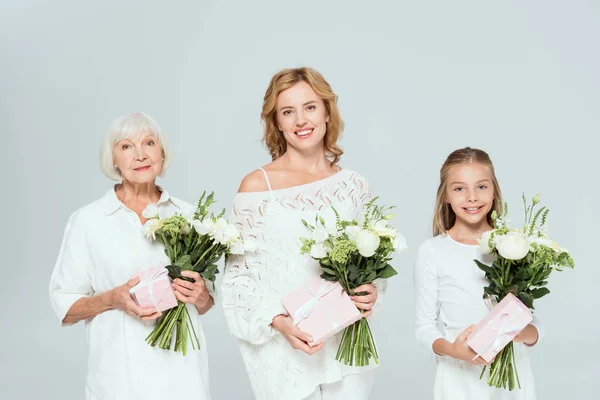 Smiling granddaughter, mother and grandmother holding bouquets and gifts isolated on grey — Stock Photo