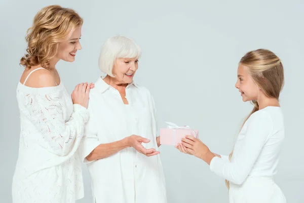 Smiling granddaughter giving gift to grandmother isolated on grey — Stock Photo