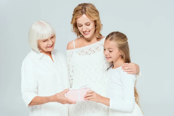 Smiling granddaughter, mother and grandmother looking at gift isolated on grey — Stock Photo