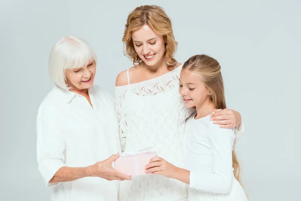 Nieta sonriente, madre y abuela mirando regalo aislado en gris - foto de stock