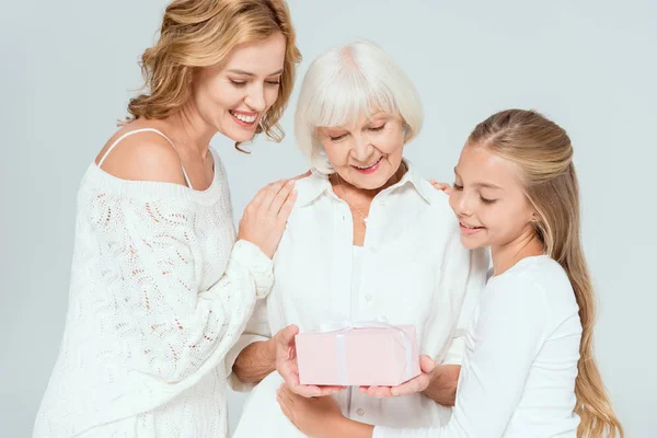 Lächelnde Enkelin, Mutter und Großmutter betrachten Geschenk isoliert auf grau — Stockfoto