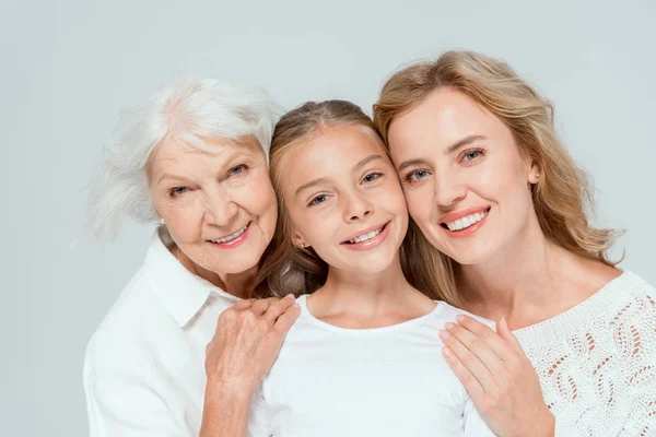 Smiling mother and grandmother hugging granddaughter isolated on grey — Stock Photo
