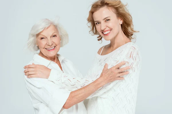 Smiling mother and daughter hugging and looking at camera isolated on grey — Stock Photo