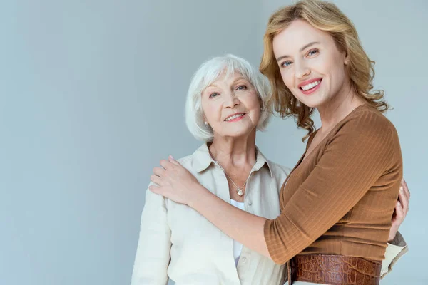 Sorridente madre e figlia che si abbracciano e guardano la telecamera isolata su grigio — Stock Photo