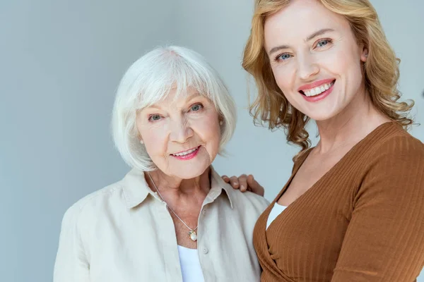 Smiling daughter hugging mother and looking at camera isolated on grey — Stock Photo