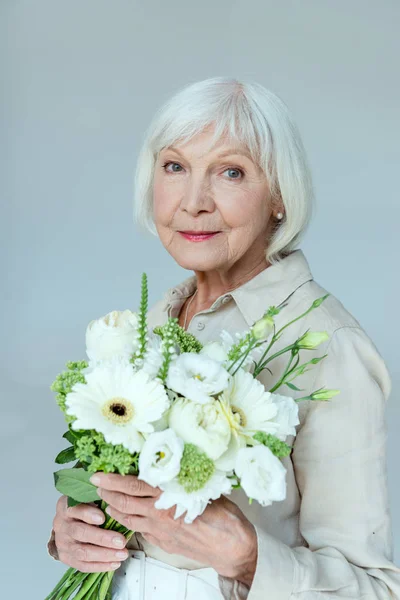 Attraktive und lächelnde Frau mit Blumenstrauß, die in die Kamera schaut, isoliert auf grau — Stockfoto