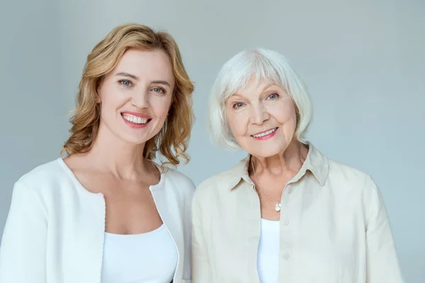 Lächelnde Mutter und Tochter blicken vereinzelt in die Kamera auf grau — Stockfoto