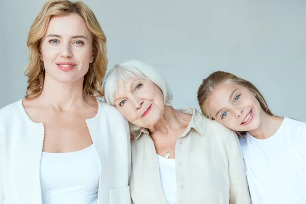 Smiling granddaughter, mother, grandmother lying on shoulders isolated on grey — Stock Photo