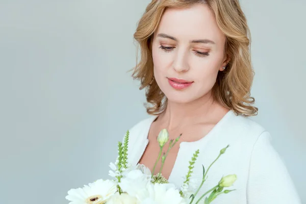 Mujer atractiva sosteniendo ramo y mirando hacia abajo aislado en gris — Stock Photo