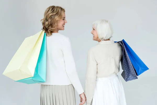 Vista trasera de la sonriente madre y su hija sosteniendo bolsas aisladas en gris - foto de stock