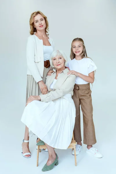 Sorridente nipote e madre che abbraccia nonna su sgabello su sfondo grigio — Foto stock