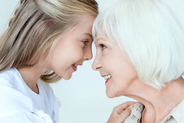 Seitenansicht von lächelnder Enkelin und Großmutter, die sich isoliert auf grau anschauen — Stockfoto