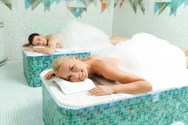 Attractive and smiling friends lying with foam in Turkish bath — Stock Photo