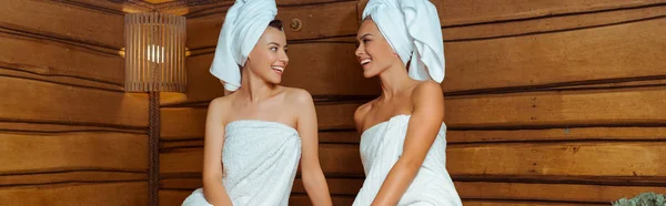 Plan panoramique d'amis souriants et attrayants en serviettes se regardant dans le sauna — Photo de stock