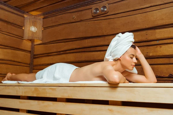 Attractive woman in towels with closed eyes lying in sauna — Stock Photo