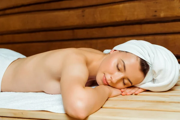 Attraente donna in asciugamani con gli occhi chiusi sdraiato in sauna — Foto stock