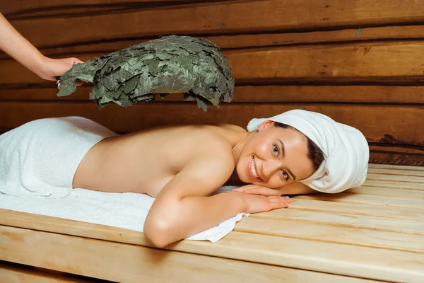 Cropped view of woman hitting her friend with birch broom in sauna — Stock Photo