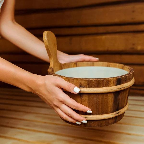 Vue recadrée d'une femme tenant une baignoire en bois dans un sauna — Photo de stock