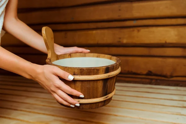 Vue recadrée d'une femme tenant une baignoire en bois dans un sauna — Photo de stock