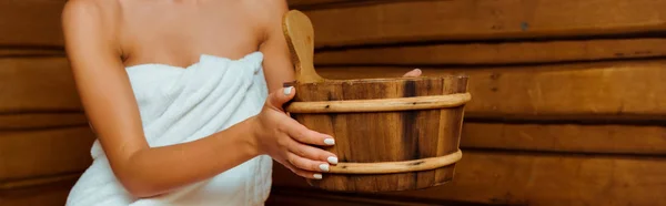 Panoramic shot of woman holding wooden washtub in sauna — Stock Photo