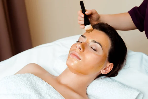 Vista cortada de cosmetologist aplicando máscara facial em mulher atraente no spa — Fotografia de Stock