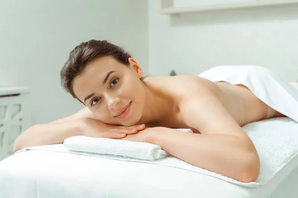 Attraktive und lächelnde Frau auf Massagetisch im Wellnessbereich liegend — Stockfoto