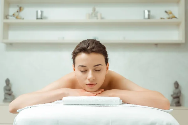 Atractiva mujer con los ojos cerrados acostada en la mesa de masaje en el spa - foto de stock