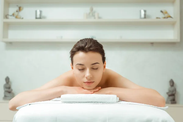 Attraktive Frau mit geschlossenen Augen auf Massagetisch im Wellnessbereich liegend — Stockfoto