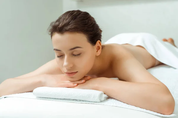 Attractive woman with closed eyes lying on massage table in spa — Stock Photo