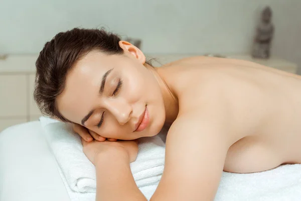 Attraktive Frau mit geschlossenen Augen auf Massagetisch im Wellnessbereich liegend — Stockfoto